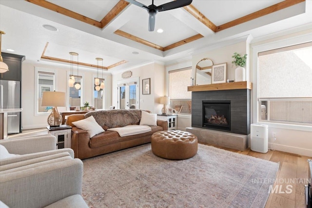 living room with beam ceiling, a glass covered fireplace, crown molding, and light wood-style floors