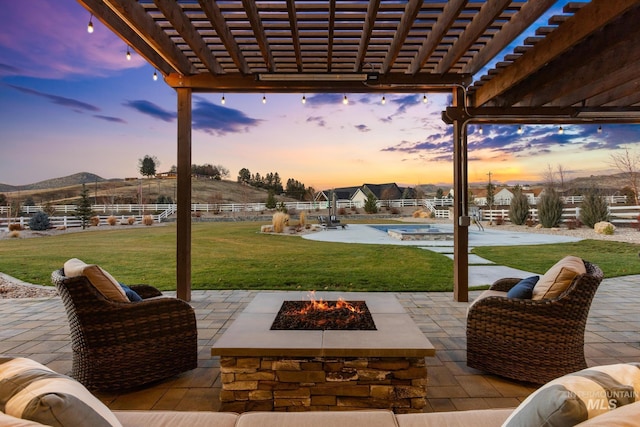 patio terrace at dusk with a pergola, an outdoor fire pit, and a lawn