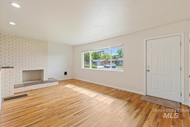 unfurnished living room featuring wood-type flooring, a textured ceiling, and a brick fireplace