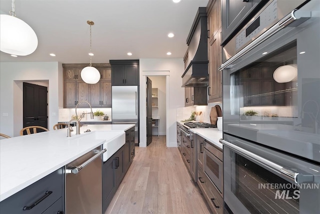 kitchen featuring a sink, stainless steel appliances, light wood-style floors, light countertops, and pendant lighting