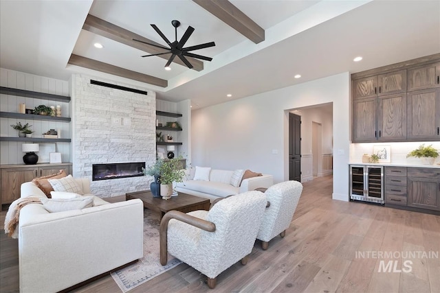 living area with bar area, beverage cooler, light wood-style floors, a fireplace, and a ceiling fan