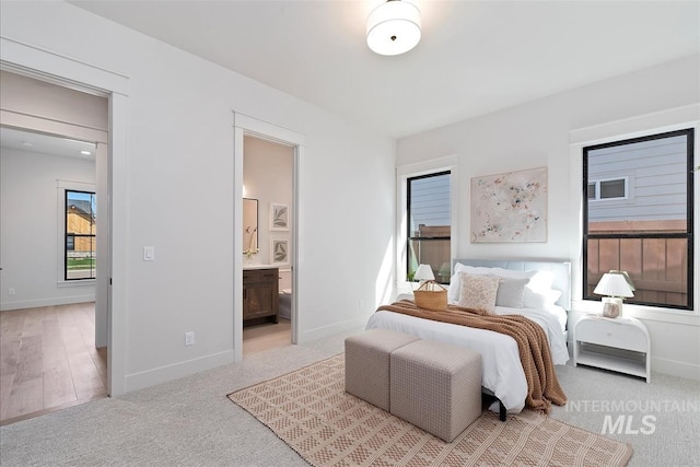 bedroom featuring baseboards, connected bathroom, and light colored carpet