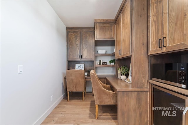 office featuring baseboards, light wood-style flooring, and built in desk