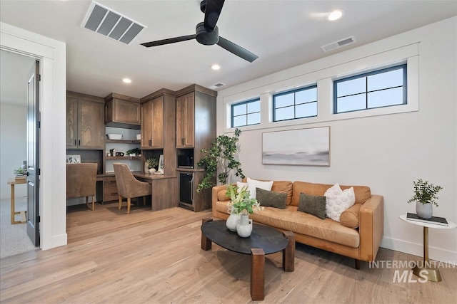 living room featuring visible vents, a ceiling fan, light wood finished floors, and built in desk