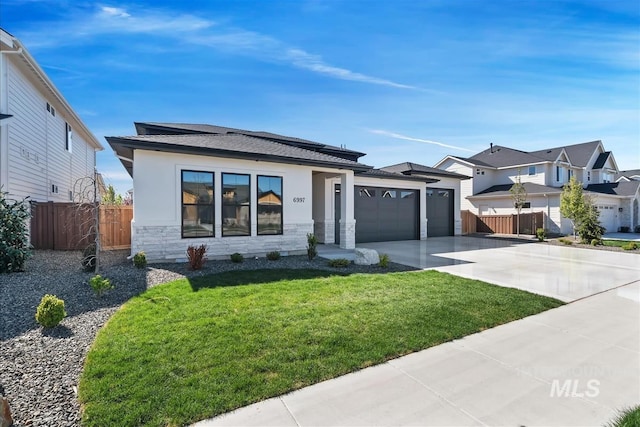 prairie-style house featuring fence, stone siding, a front lawn, concrete driveway, and an attached garage