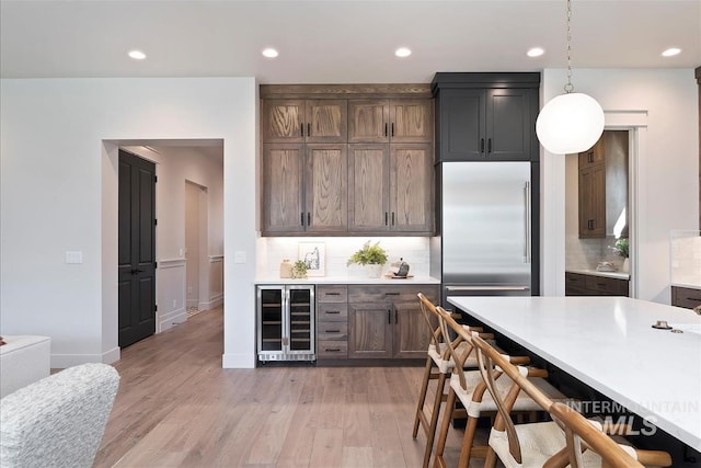 kitchen with beverage cooler, built in fridge, light countertops, recessed lighting, and backsplash