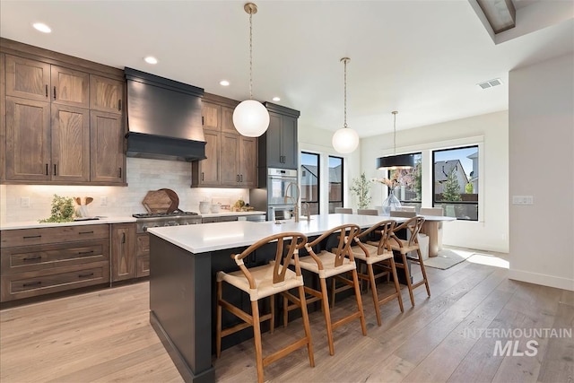 kitchen featuring custom range hood, a breakfast bar, visible vents, light countertops, and appliances with stainless steel finishes
