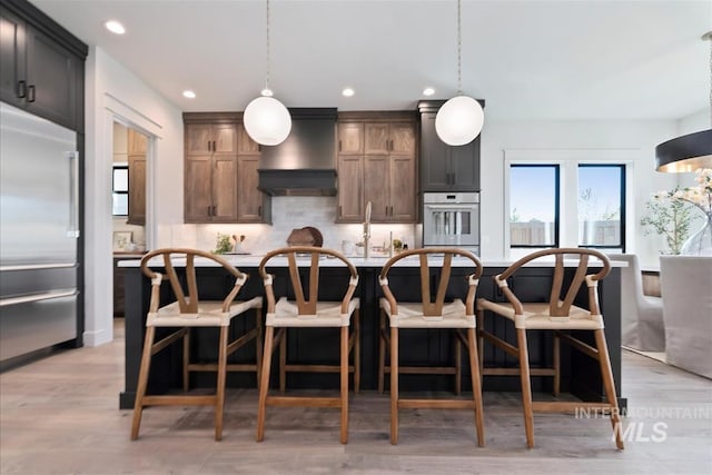 kitchen featuring recessed lighting, decorative backsplash, a breakfast bar, appliances with stainless steel finishes, and premium range hood
