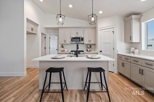 kitchen with a breakfast bar, light countertops, stainless steel microwave, light wood-style floors, and a kitchen island with sink