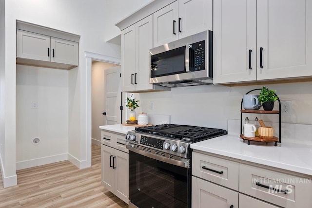 kitchen featuring stainless steel appliances, baseboards, light countertops, and light wood finished floors