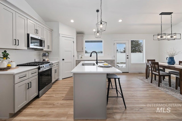 kitchen featuring stainless steel appliances, light countertops, hanging light fixtures, a sink, and an island with sink