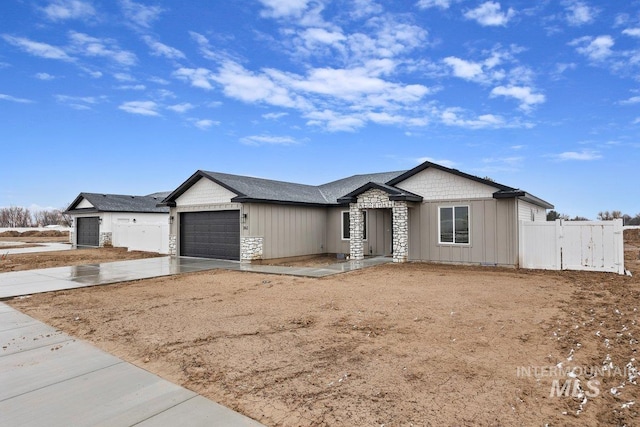 view of front of property featuring concrete driveway, stone siding, an attached garage, fence, and board and batten siding