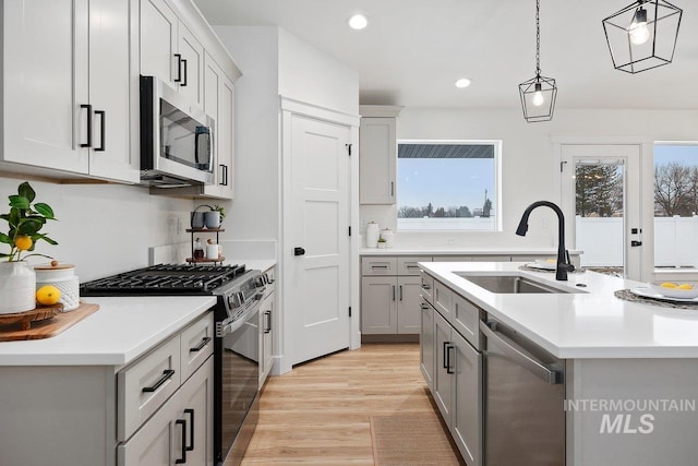 kitchen featuring appliances with stainless steel finishes, gray cabinets, light countertops, pendant lighting, and a sink