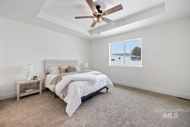 carpeted bedroom with ceiling fan, a raised ceiling, visible vents, and baseboards