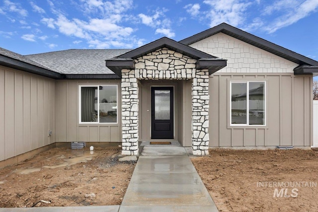 doorway to property featuring board and batten siding, stone siding, and a shingled roof