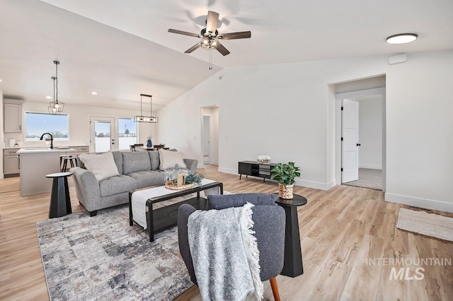 living area with lofted ceiling, light wood finished floors, ceiling fan, and baseboards