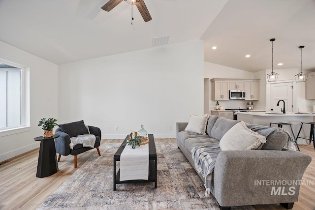 living area featuring lofted ceiling, a ceiling fan, visible vents, baseboards, and light wood-type flooring