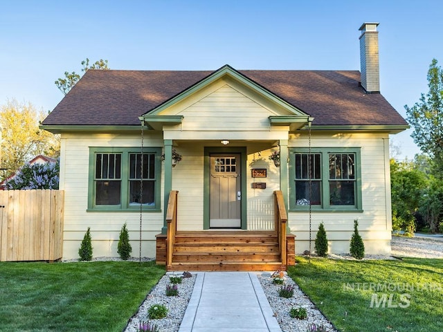 bungalow-style house featuring a front lawn, roof with shingles, fence, and a chimney