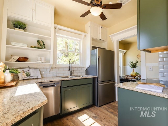 kitchen featuring a ceiling fan, appliances with stainless steel finishes, wood finished floors, a sink, and light stone counters
