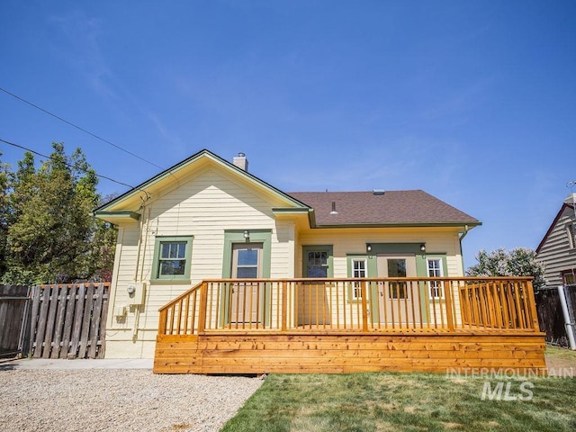 back of house with roof with shingles, fence, and a deck