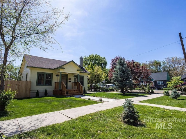 bungalow-style house with a porch, fence, a front yard, and a chimney