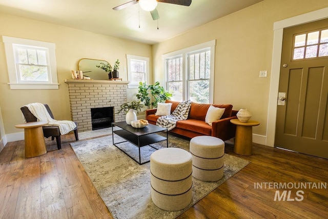 living area featuring baseboards, a ceiling fan, a fireplace, and hardwood / wood-style floors