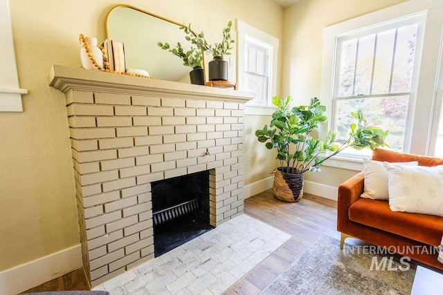 living area with baseboards, wood finished floors, a healthy amount of sunlight, and a fireplace