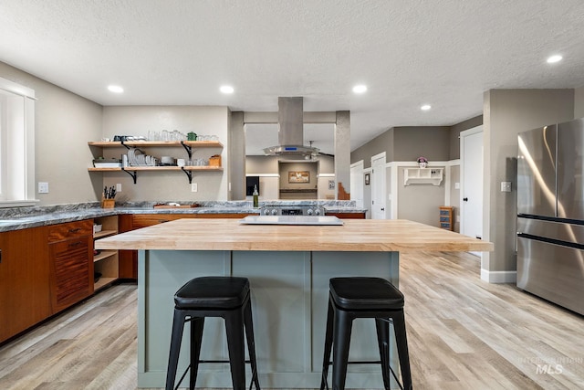 kitchen with island exhaust hood, butcher block countertops, a breakfast bar, and freestanding refrigerator