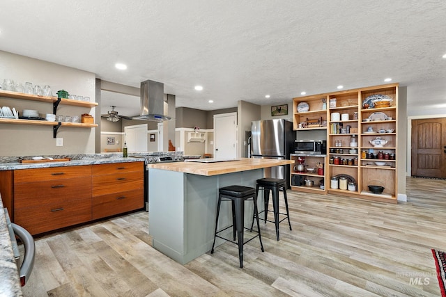 kitchen featuring open shelves, light wood-style flooring, appliances with stainless steel finishes, wood counters, and wall chimney exhaust hood