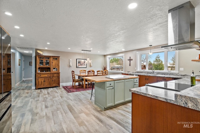 kitchen with light wood-style flooring, wood counters, a kitchen breakfast bar, wall chimney exhaust hood, and green cabinetry