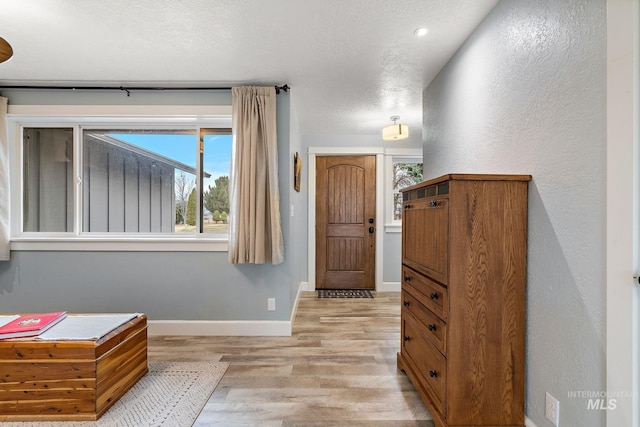 foyer featuring baseboards, a textured ceiling, and light wood-style flooring