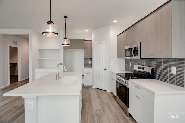 kitchen featuring light wood finished floors, stainless steel appliances, light countertops, open shelves, and a sink