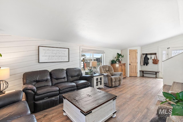 living room featuring wood-type flooring, lofted ceiling, and wooden walls