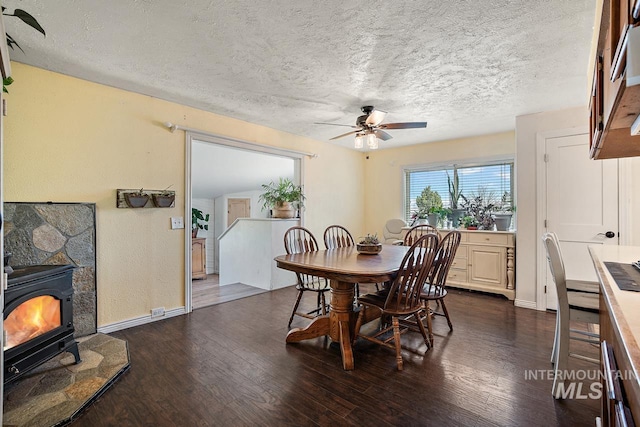 dining space with a wood stove, ceiling fan, dark wood-type flooring, and a textured ceiling