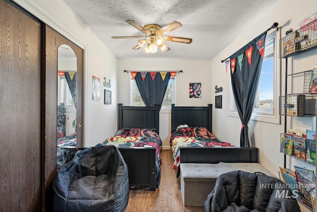 bedroom with a textured ceiling, hardwood / wood-style flooring, multiple windows, and ceiling fan