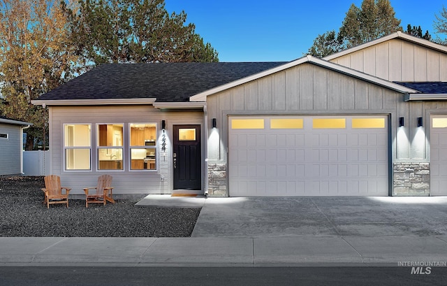 view of front facade with a garage, stone siding, roof with shingles, and board and batten siding