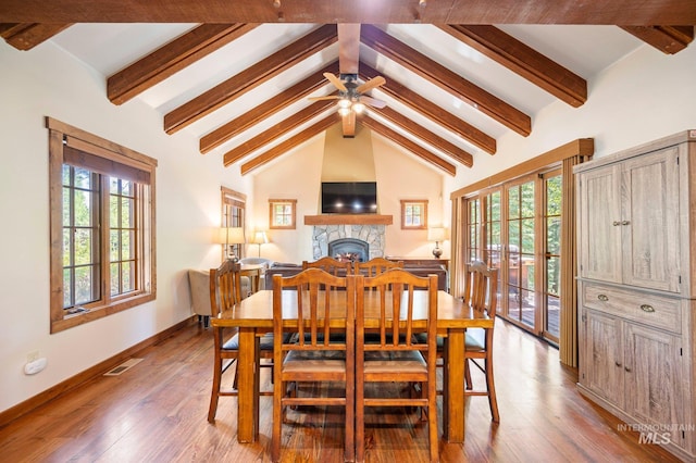 dining area featuring hardwood / wood-style floors, beamed ceiling, high vaulted ceiling, ceiling fan, and a stone fireplace