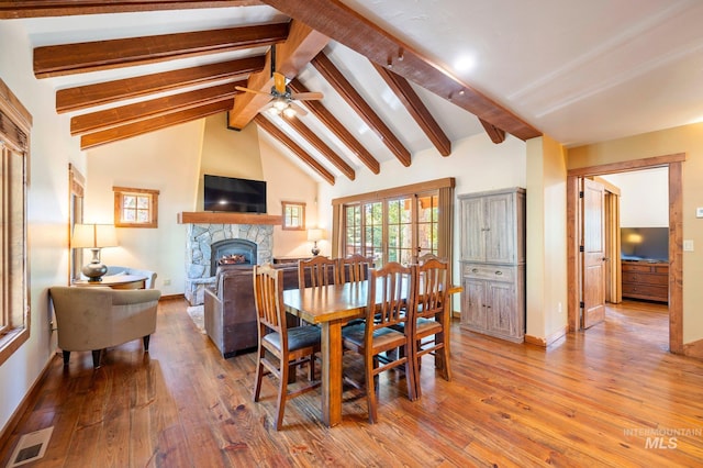 dining area with beam ceiling, high vaulted ceiling, ceiling fan, a stone fireplace, and hardwood / wood-style flooring