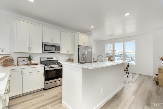 kitchen featuring hanging light fixtures, a center island with sink, stainless steel appliances, light hardwood / wood-style floors, and white cabinets