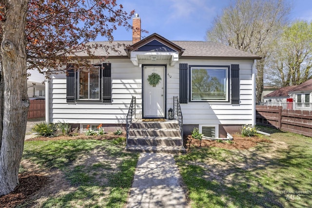 bungalow-style house with fence, a shingled roof, and a chimney