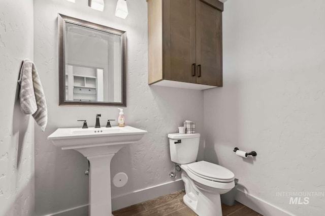 half bath featuring baseboards, toilet, and wood finished floors