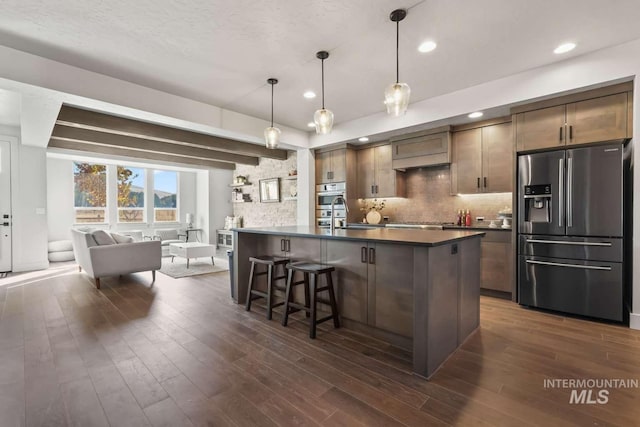 kitchen with a breakfast bar area, dark wood-style flooring, appliances with stainless steel finishes, dark countertops, and backsplash