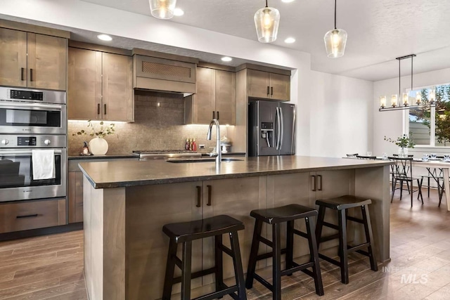 kitchen featuring a sink, backsplash, appliances with stainless steel finishes, and wood finished floors