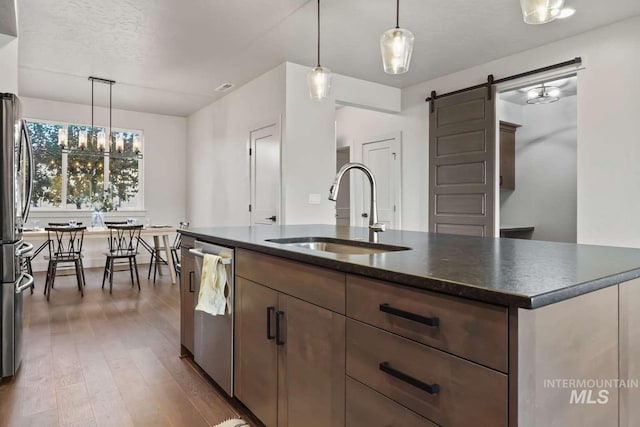 kitchen with wood finished floors, a sink, pendant lighting, dishwasher, and a barn door