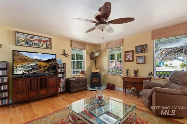 living room featuring wood-type flooring, a wood stove, and ceiling fan