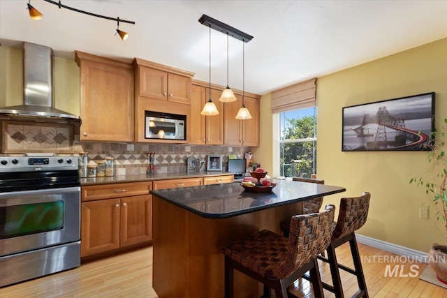 kitchen featuring track lighting, appliances with stainless steel finishes, wall chimney exhaust hood, and light hardwood / wood-style flooring