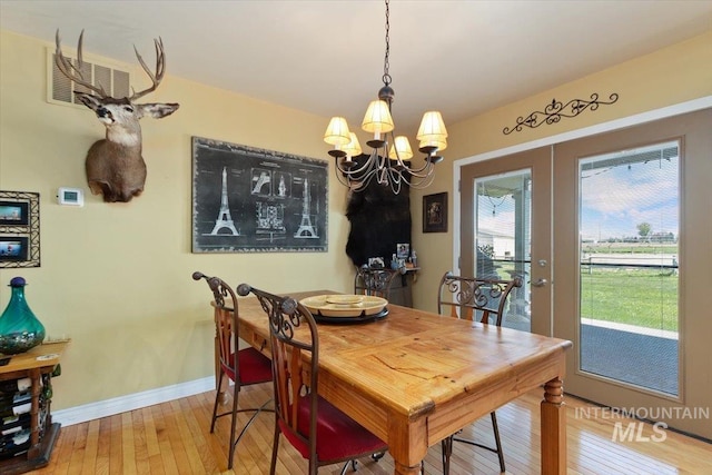 dining area with wood-type flooring, an inviting chandelier, and french doors