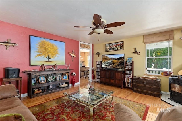 living room with wood-type flooring, ceiling fan, and a wood stove