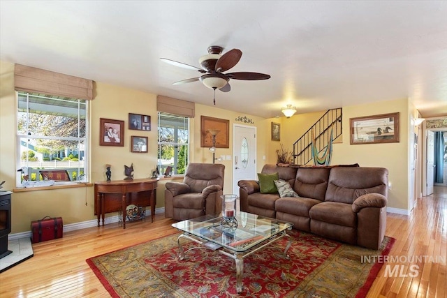 living room with ceiling fan, a wood stove, and light hardwood / wood-style flooring