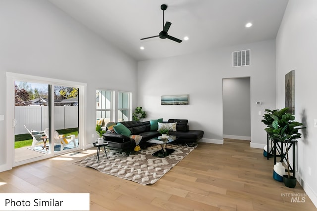 living area featuring light wood-type flooring, visible vents, baseboards, and high vaulted ceiling